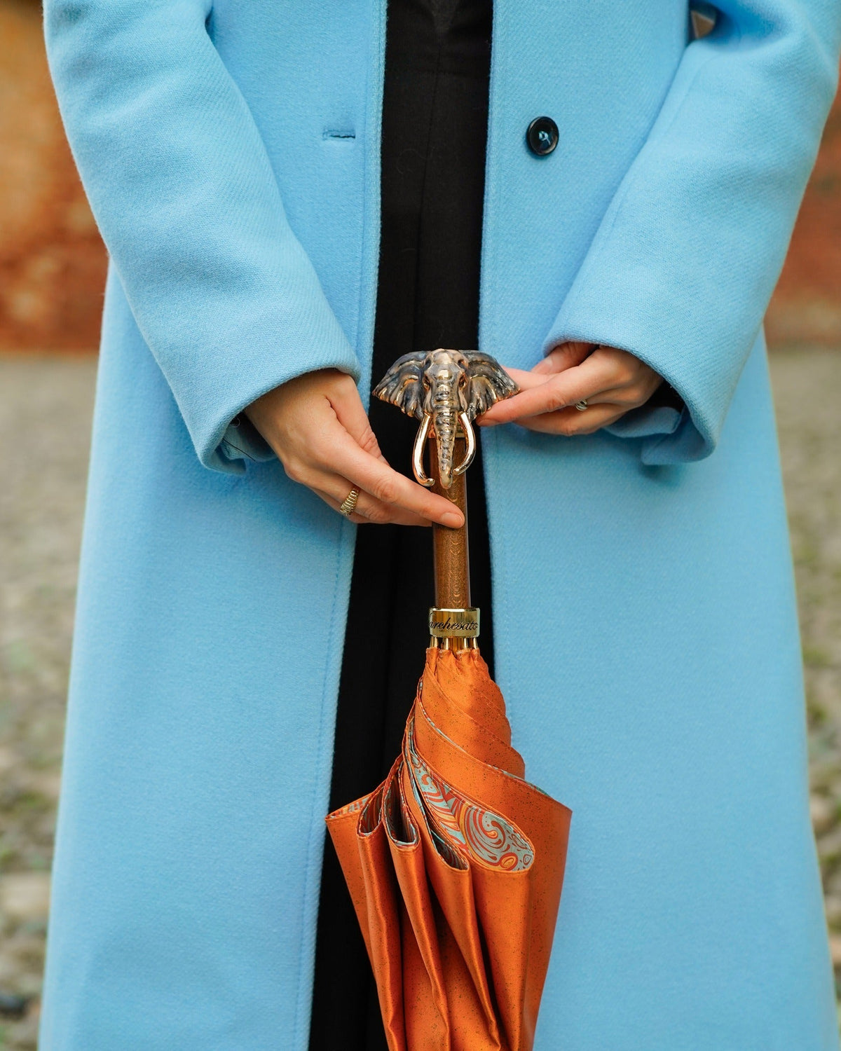 Woman in a blue coat holding a folded umbrella with an elephant-head handle