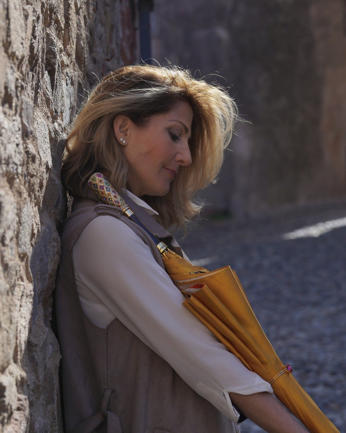 Woman leaning against a stone wall in an Italian alley holding an umbrella
