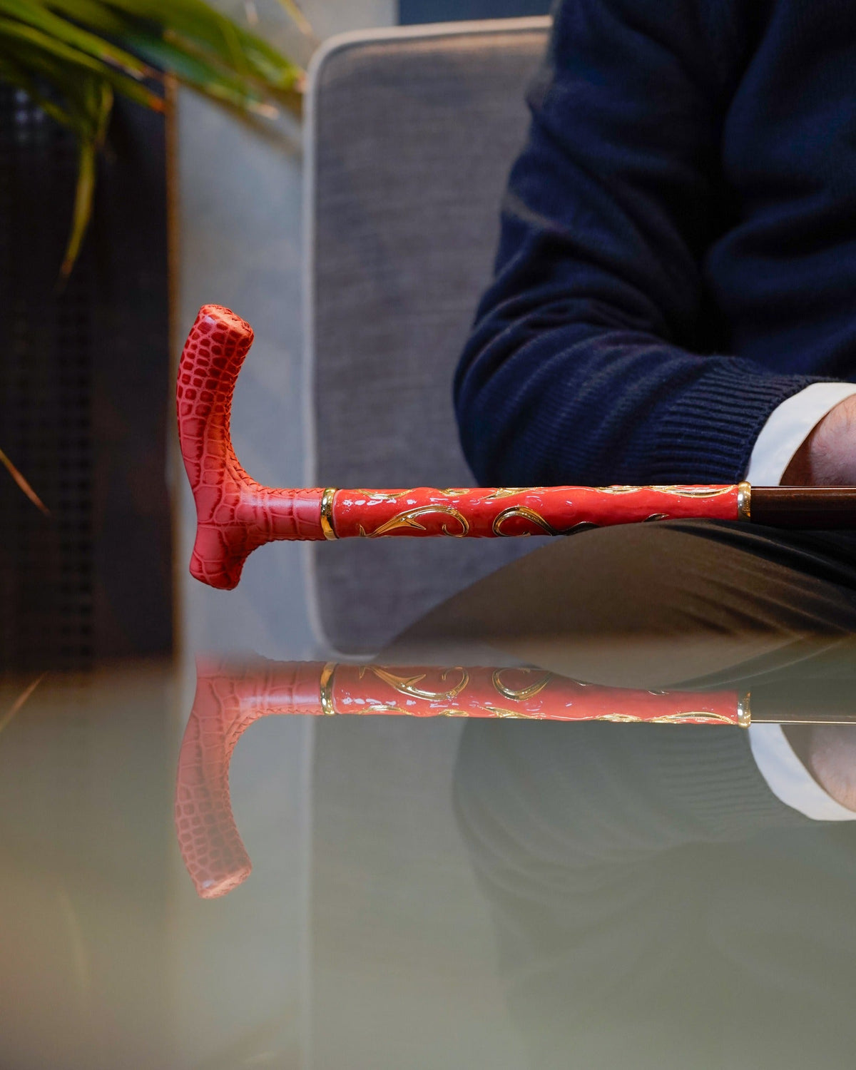 Man seated holding a walking cane handle at a glass table, showing cane proportion