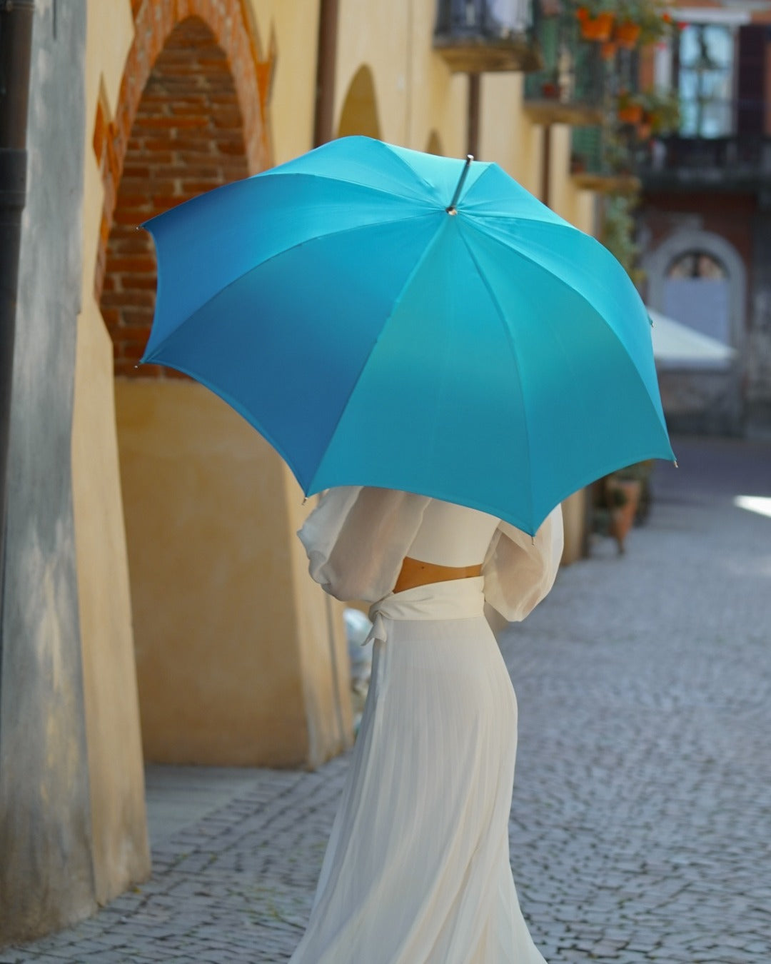 Woman walking under a fully open blue umbrella on an Italian street