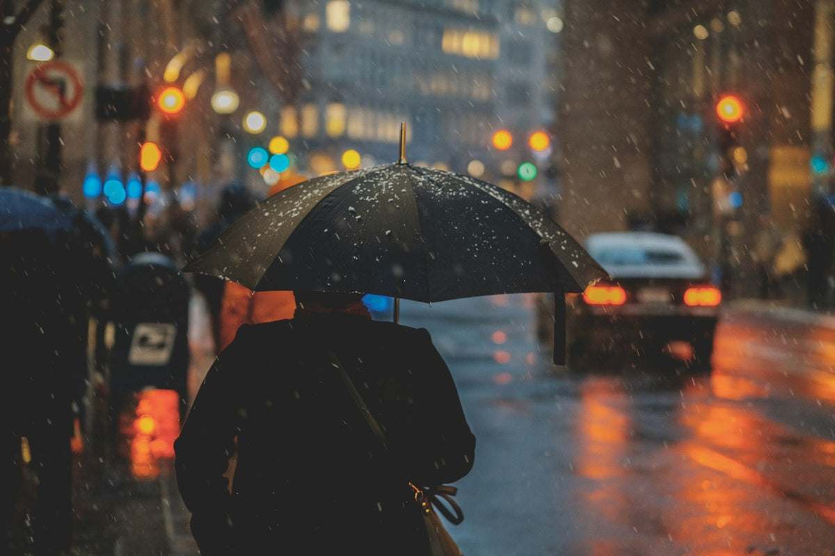 Person walking on a rainy city street at night holding an umbrella, car lights blurred in the background