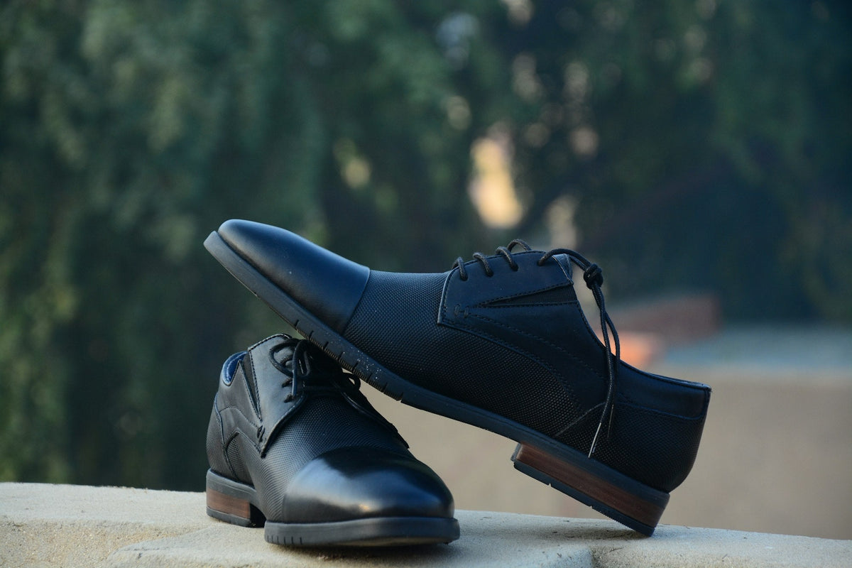 Pair of polished black leather dress shoes resting on a stone ledge
