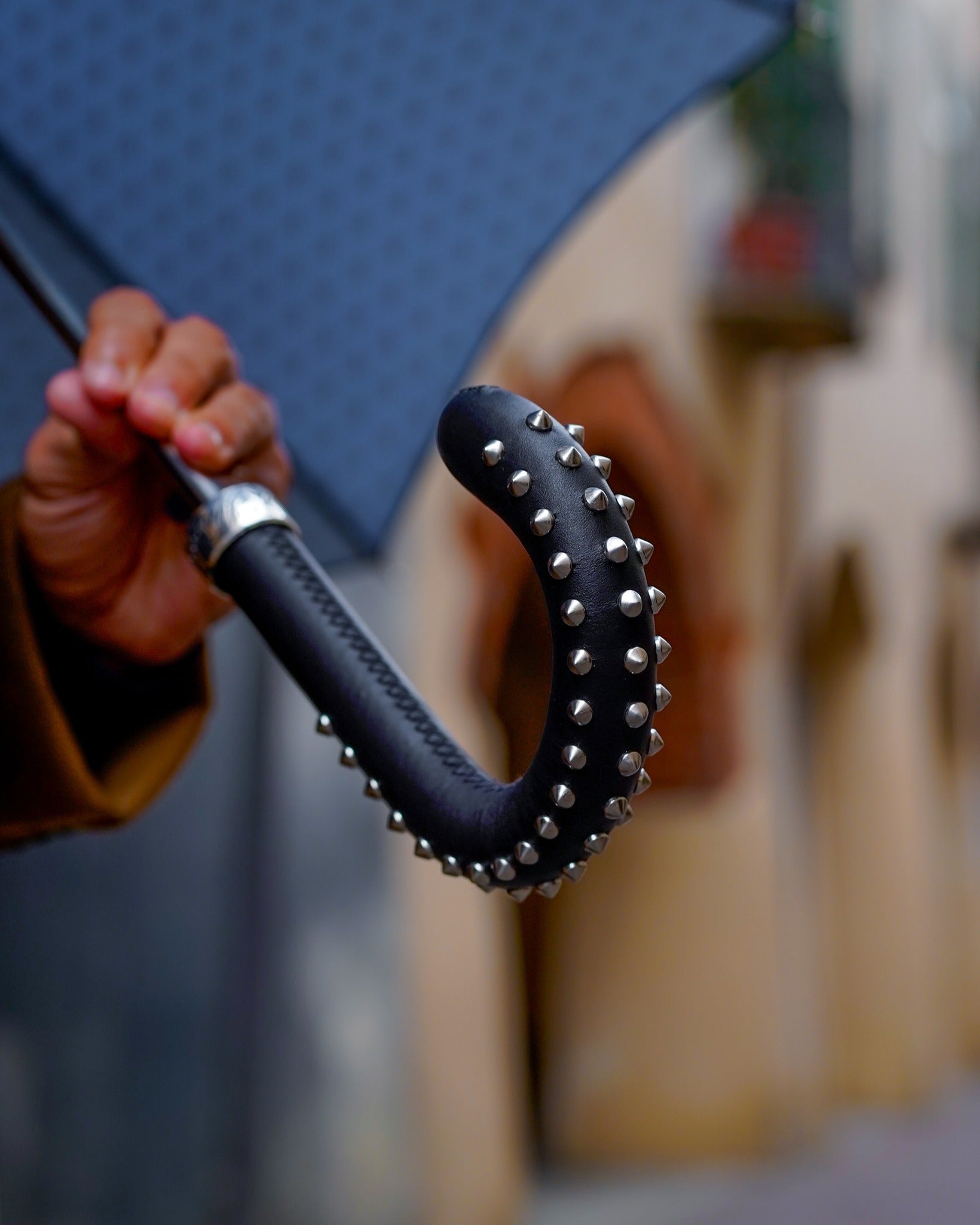 Men's premium Ilmarchesato umbrella with rock-style studded leather handle and durable carbon fiber ribs, open in a natural setting.